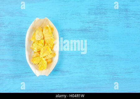 Getrocknete Ananas Scheiben in einer Holzschale auf einem rustikalen Tisch Platz für Text, Ansicht von oben. Stockfoto