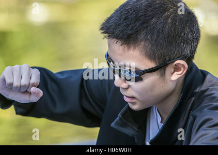 Ein Junge macht eine Bewegung während einer Partie Schach. Das Schachbrett spiegelt sich in seine Sonnenbrille. Stockfoto