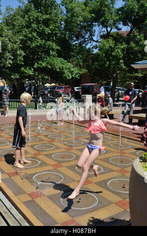 Mädchen springt über Wasserdüse an die Kinder-Wasser-Funktion auf Pearl Street Mall Stockfoto