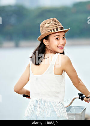 junge und schöne Asiatin mit Blick auf Kamera Lächeln während der Fahrt mit dem Fahrrad Stockfoto