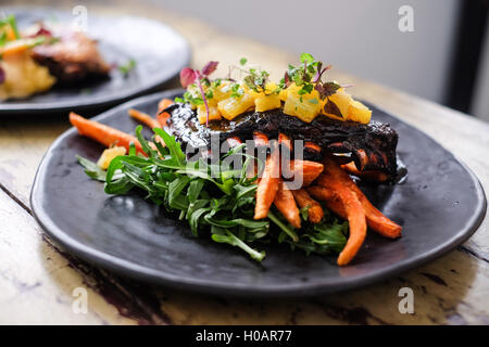 Gebratenes Schweinefleisch mit Kartoffeln und Kräutern auf schwarze Platte Rippen Stockfoto