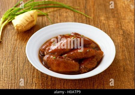 Gebratene Hähnchenflügel auf weißen Teller auf Holztablett mit Ingwer und Zwiebeln Stockfoto