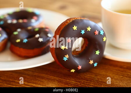 Schokolade Donut mit Wachspapier und Getränk auf Holztisch Schokolade Donut mit Wachspapier und Getränk auf Holztisch