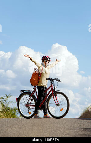Frau Radfahrer stehen mit dem Fahrrad auf der Straße Horizont und die Hände zum Himmel emporgehoben. Stockfoto