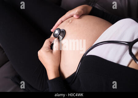 Schwangere Frau hören Babys Herzschlag mit Stethoskop auf den Bauch gelegt hautnah Stockfoto