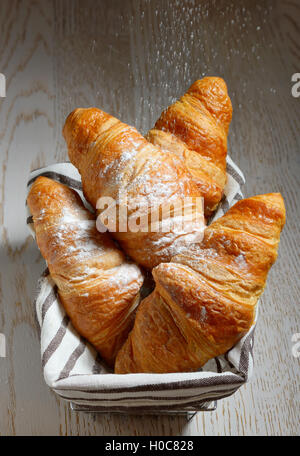 Leckere Croissants in Korb auf hölzernen Hintergrund Stockfoto