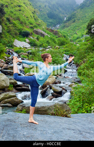 Frau tut Yoga Asana Natarajasana im Freien am Wasserfall Stockfoto