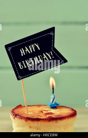 Nahaufnahme von einem Käsekuchen garniert mit eine schwarze Flagge-förmigen Schild mit dem Text happy Birthday geschrieben und einen beleuchteten Geburtstag Stockfoto