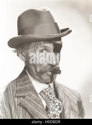 Mann mit Augenklappe und Fedora rauchende Zigarre Stockfoto