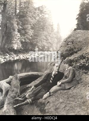 Paar sitzt auf Felsen neben Bach Stockfoto