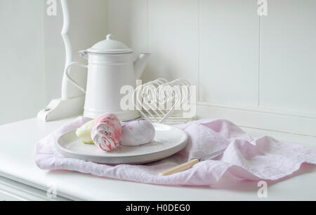 In Pastelltönen gestalteten Meringue Foto auf einem weißen Küche Sideboard mit einem weißen Emaille Kaffeekanne gestaltet. Pastell rosa Bettwäsche Serviette in den Schuß. Stockfoto