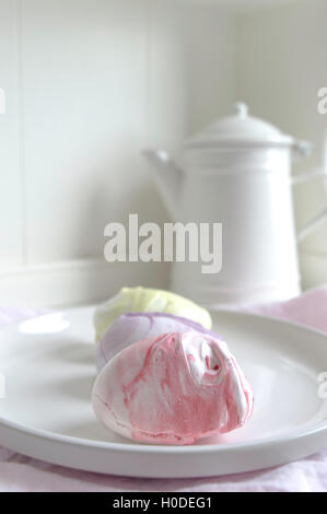 In Pastelltönen gestalteten Meringue Foto auf einem weißen Küche Sideboard mit einem weißen Emaille Kaffeekanne gestaltet. Pastell rosa Bettwäsche Serviette in den Schuß. Stockfoto