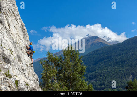 Schlanke männliche Kletterer in blau auf steilen Felswand mit blauem Himmel Berge und Wolken Stockfoto