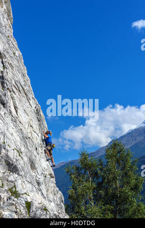 Schlanke männliche Kletterer in blau auf steilen Felswand mit blauem Himmel Berge und Wolken Stockfoto