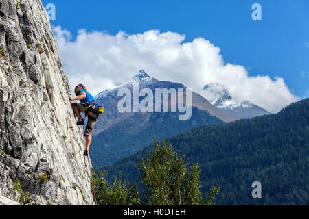 Schlanke männliche Kletterer in blau auf steilen Felswand mit blauem Himmel Berge und Wolken Stockfoto