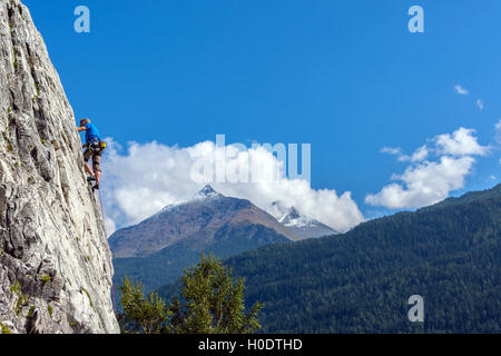 Schlanke männliche Kletterer in blau auf steilen Felswand mit blauem Himmel Berge und Wolken Stockfoto