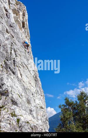 Schlanke männliche Kletterer in blau auf steilen Felswand mit blauem Himmel Berge und Wolken Stockfoto