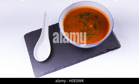 Tomatencremesuppe mit Shrimps auf schwarzen Felsplatte auf weißem Hintergrund Stockfoto