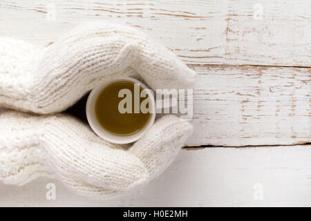 Weibes Hände in Handschuhe halten eine Tasse Tee weißer Holztisch Stockfoto