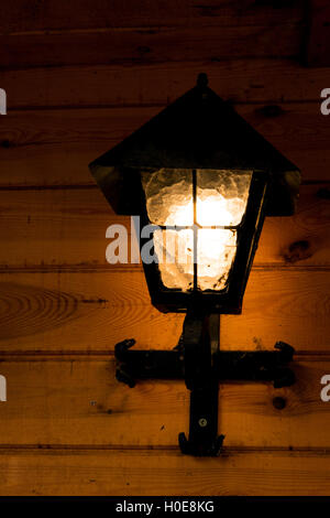 Glänzend, alte Metall Lampe montiert auf einer Holzwand Holzgebäude, Sommerabend. Vertikale Ansicht. Stockfoto