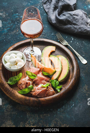 Mozzarella-Käse in die Schüssel, Prosciutto di Parma, Cantloupe Melonenscheiben und Glas Rosé auf Runde Holz Serviertablett über Stockfoto