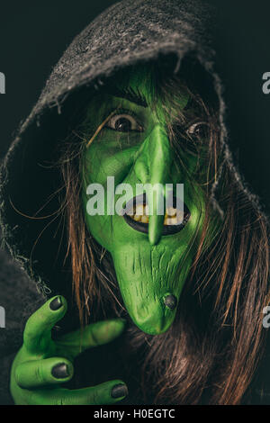 Grüne Hexe mit dunklen Kapuze zu handeln, wie sie einen Fluch wirft. Geringe Schärfentiefe. Stockfoto