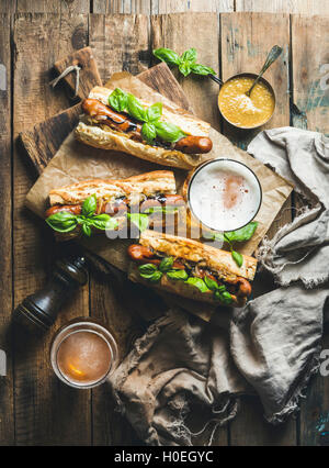 Gläser des Weizens ungefiltertes Bier und gegrillten Würstchen Hunde in Baguette mit Senf, karamellisierten Zwiebeln und Kräutern auf dem board Stockfoto