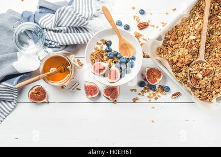 Gesunden Frühstücks-Set. Hafer-Müsli mit Nüssen, Joghurt, Honig, frische Feigen und Heidelbeeren in Schüssel auf weißem Holz Hintergrund, top Stockfoto