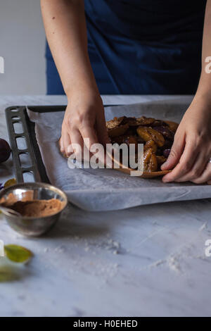 Frau Falten Teig über geschnittene Pflaumen, Zutaten für das Backen Pflaume galette Stockfoto