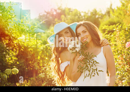 Zwei Schwestern. Mädchen mit einem Blumenstrauß. Schwester im Hintergrund umarmt sie. Zeit mit der Familie. Menschliche Beziehungen. Stockfoto