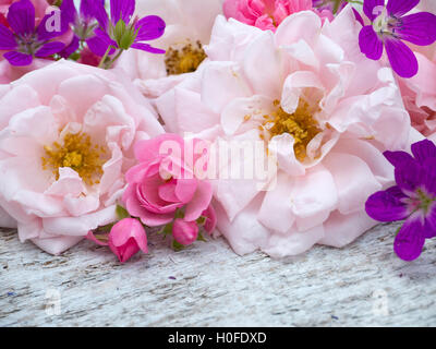 Großen blass rosa und kleine leuchtend rosa Rosen und Geranien Bouquet auf dem weißen groben Holztisch Stockfoto