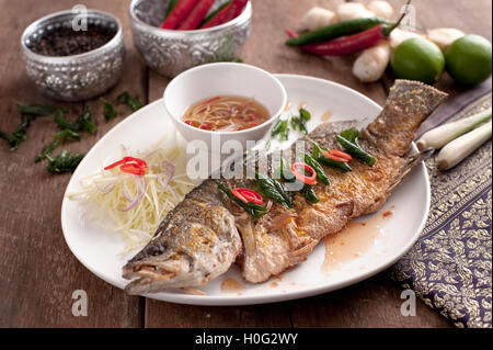 Gebratener Barramundi Fisch mit Fisch-Sauce auf weißen Teller mit Zitrone, Chili und Zitronengras Stockfoto