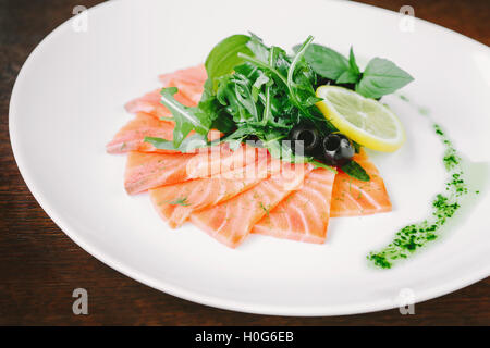 Unter Rühren gebraten in Scheiben geschnittenen Lachs mit Olivenöl, Zitrone und Kräutern auf weißen Teller Stockfoto