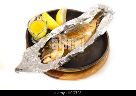 Gegrillter Fisch in Folie Uith Zitrone Saft Soße in schwarze Pfanne auf Holzbrett Stockfoto