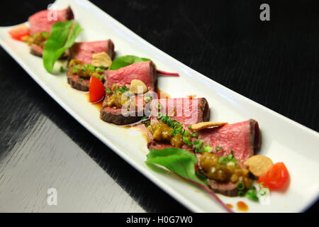 Rindersteak mit Zwiebeln, Tomaten und Gewürzen auf weißen Teller geschnitten Stockfoto