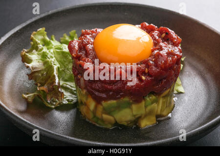 Avocado-Tartar Stich Sakura Rindfleisch mit roten Ei und Salat auf schwarzem Teller Stockfoto