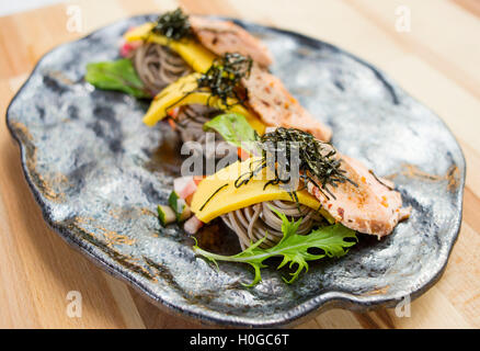 Lachs Soba mit Nudeln, Kräuter und Algen auf schwarzem Teller Stockfoto