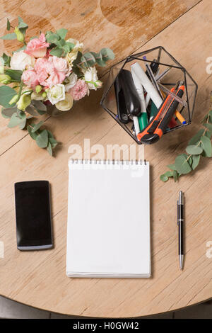 Notizblock mit Stift und Schwarz Smartphone auf Holztisch im Coffee-Shop in Morgen Szene geöffnet. Ansicht von oben Stockfoto