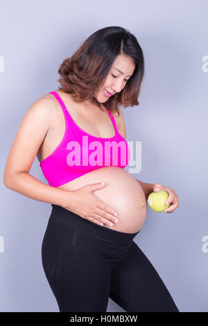 Schöne schwangere Frau mit grünem Apfel auf grauem Hintergrund Stockfoto