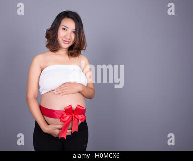 Schwangere Frau mit roten Schleife Geschenk auf Bauch Stockfoto