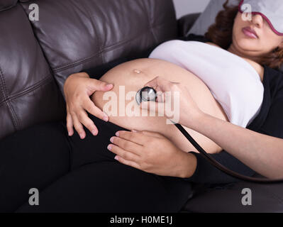 Nahaufnahme Stethoskop hören von schwangeren Bauch auf sofa Stockfoto