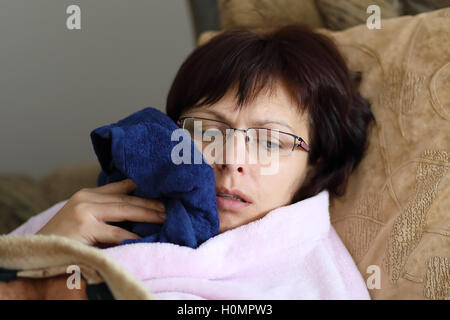 müde Frau mittleren Alters nach Narkose ziehen Weisheitszähne kühlt Ihr Gesicht entspannen und Lügen zu Hause ohne Make-up in rosa Stockfoto
