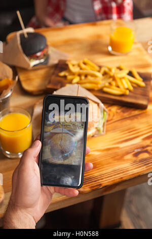 Hand des Mannes Foto von Rindfleisch Burger Gebratene Kartoffel-Fast-Food In Papier Holztisch Cafe serviert Stockfoto