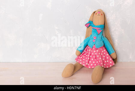 Spielzeug-Hase sitzend auf dem Holzboden vor dem Hintergrund einer blauen Wand Stockfoto