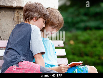 Zwei Jungs sitzen auf Bank mit Tablet spielen Stockfoto
