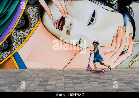 Eine bunte Graffity mit japanischen Motiv ist an einer Hauswand gemalt, ein kleines Mädchen wird auf einen Kinder Roller vorbei Stockfoto