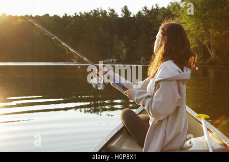 Mädchen mit Angelrute in einem Kanu auf einem See in Vermont als die Sonne aufgeht Stockfoto