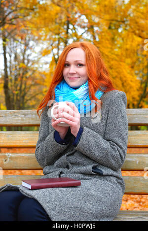 Mädchen-Porträt mit Cup und Buch über gelbe Blätter Hintergrund, Herbst Stockfoto