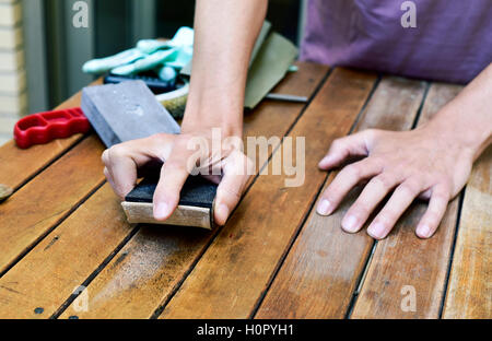 Closeup von einem kaukasischen Jüngling Schleifen einen alten Holztisch mit einem Schleifblock Stockfoto