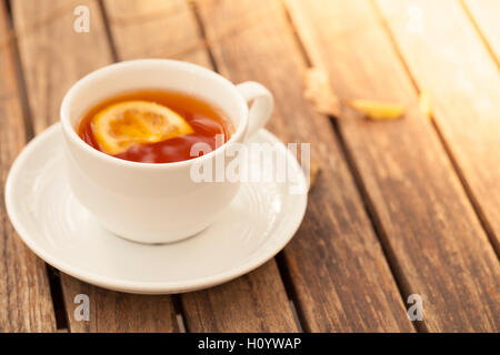 Eine Tasse Tee mit Zitrone auf dem Holztisch mit gefallenen Herbst Blätter Stockfoto